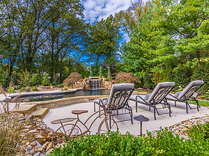 st. louis custom designed freeform concrete pool, boulder water feature with grotto, raised wall with stone veneer, lounge chairs, decorative bicycle